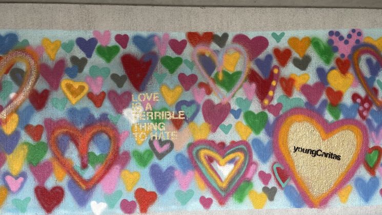 Graffiti mit bunten Herzen und der Aufschrift "Liebe ist eine schreckliche Sache zu hassen" auf einer Wand.