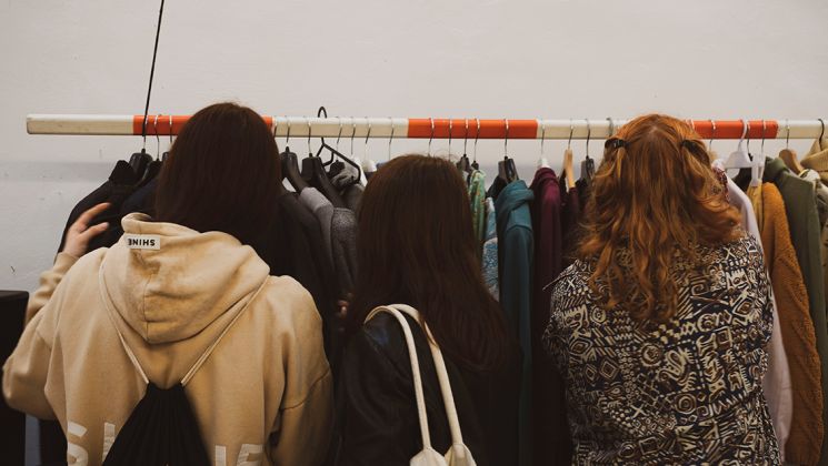 Drei Frauen stehen vor einem Kleiderständer und durchsuchen verschiedene Kleidungsteile.