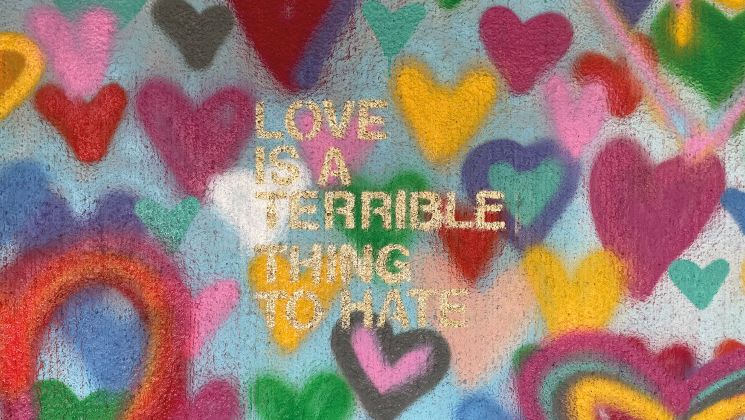 Ein graffitiartiges Kunstwerk mit Herzen in verschiedenen Farben, das den Satz 'Liebe ist eine schreckliche Sache zu hassen' zeigt.