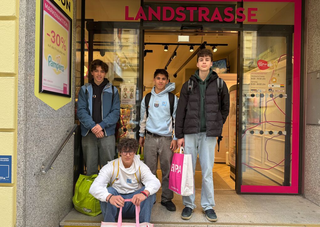 Vier Jugendliche stehen vor einem Geschäft mit bunten Einkaufstaschen. Ein Junge sitzt auf der Treppe.