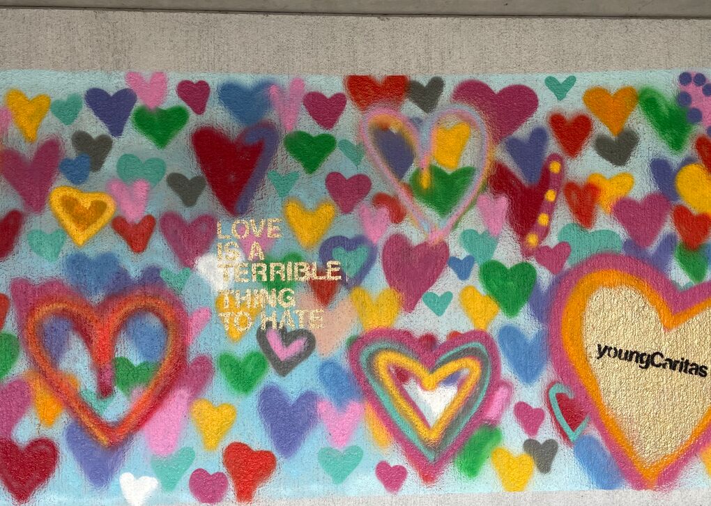 Graffiti mit bunten Herzen und der Aufschrift "Liebe ist eine schreckliche Sache zu hassen" auf einer Wand.