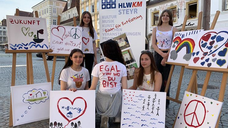 Gruppe von Jugendlichen zeigt ihre Kunstwerke mit Botschaften über Frieden und Zukunft, während sie in der Stadt stehen.