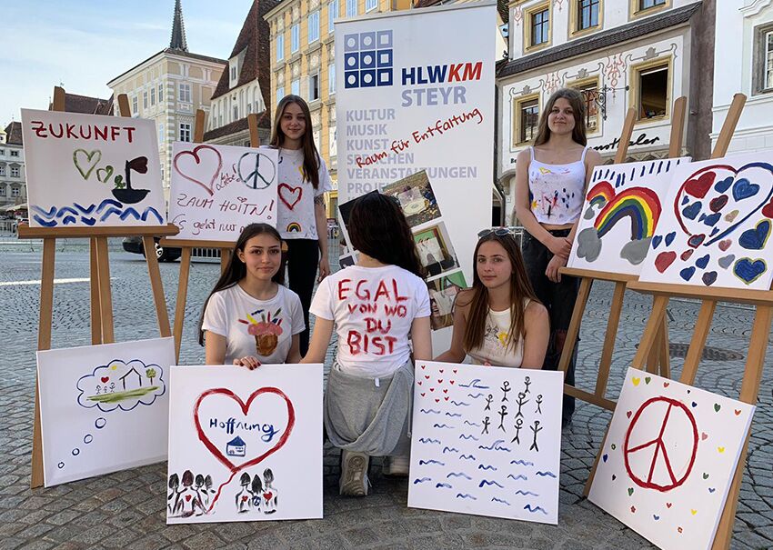 Gruppe von Jugendlichen zeigt ihre Kunstwerke mit Botschaften über Frieden und Zukunft, während sie in der Stadt stehen.