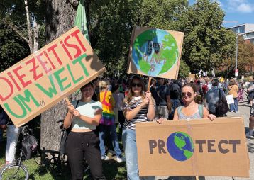 Drei Frauen halten Schilder für den Umweltschutz bei einer Demonstration. Auf den Schildern stehen wichtige Botschaften über unseren Planeten.