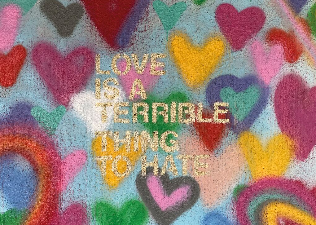 Ein graffitiartiges Kunstwerk mit Herzen in verschiedenen Farben, das den Satz 'Liebe ist eine schreckliche Sache zu hassen' zeigt.