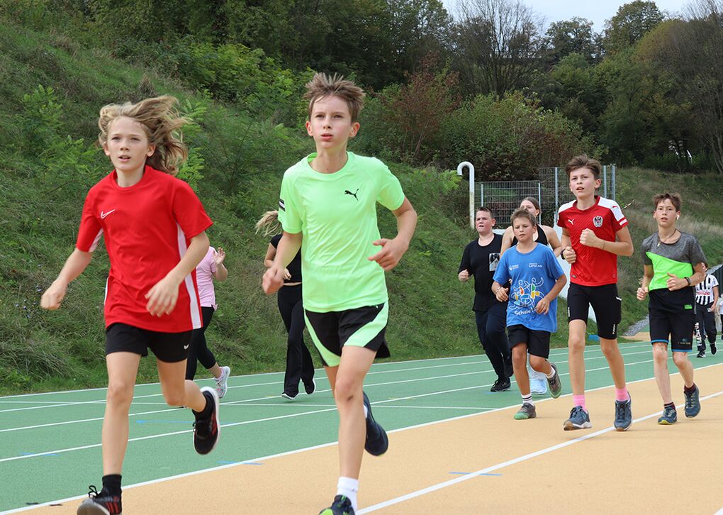 Eine Gruppe von Schülern in Sportkleidung läuft auf einer Laufbahn im Freien.