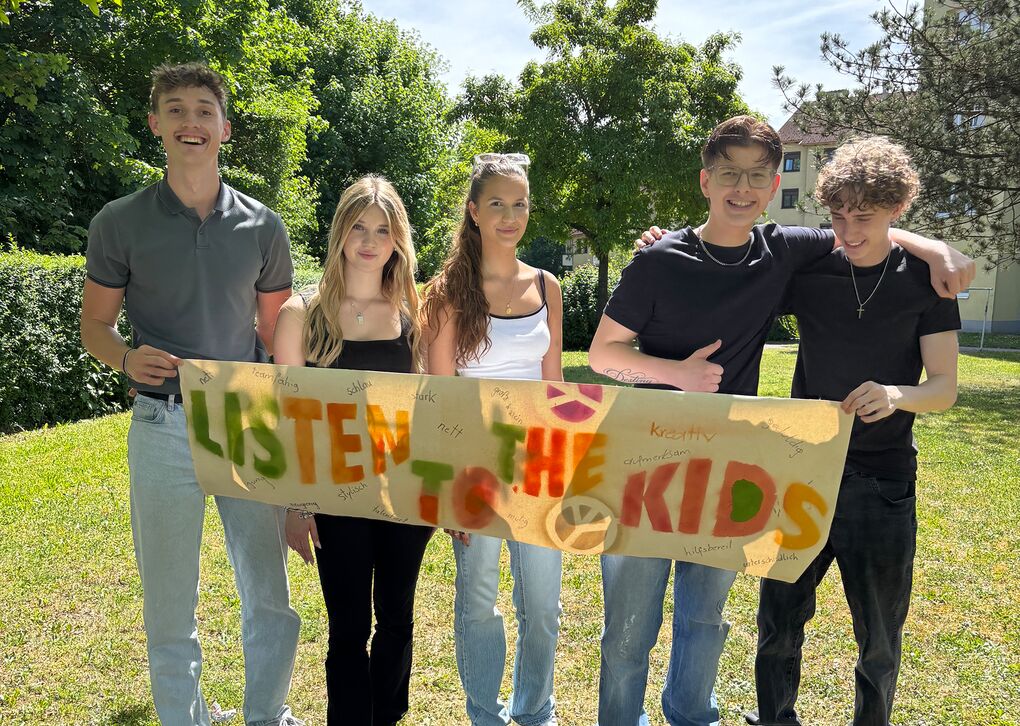 Fünf Jugendliche mit einem Plakat mit der Beschriftung "Listen to the Kids"