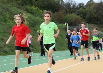 Eine Gruppe von Schülern in Sportkleidung läuft auf einer Laufbahn im Freien.
