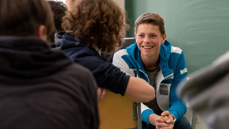 Ein Schüler lächelt und unterhält sich mit anderen Schülern in einem Klassenzimmer.