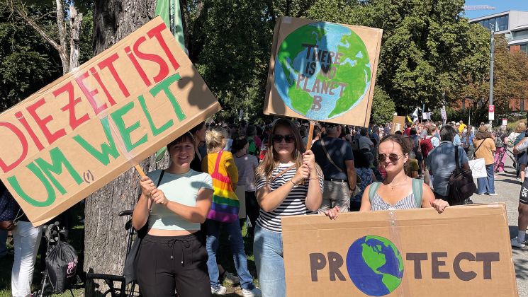Drei Frauen halten Schilder für den Umweltschutz bei einer Demonstration. Auf den Schildern stehen wichtige Botschaften über unseren Planeten.