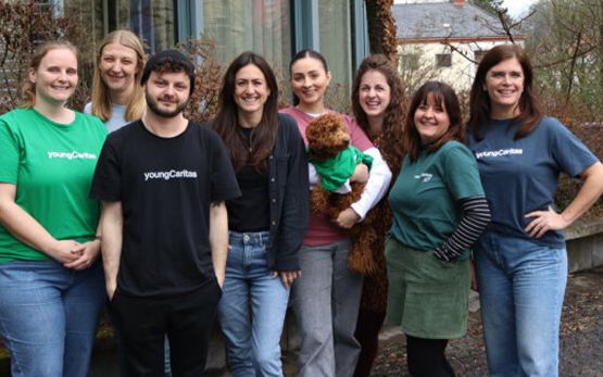 Eine Gruppe von jungen Menschen in T-Shirts von youngCaritas, die lächeln und einen Stoffhund halten.