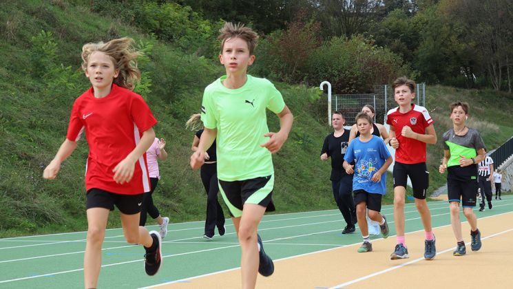Eine Gruppe von Schülern in Sportkleidung läuft auf einer Laufbahn im Freien.